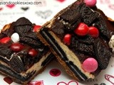 Oreo cheesecake bars on a chocolate chip cookie crust topped with a chocolate glaze, raspberry m & m’s and more oreos